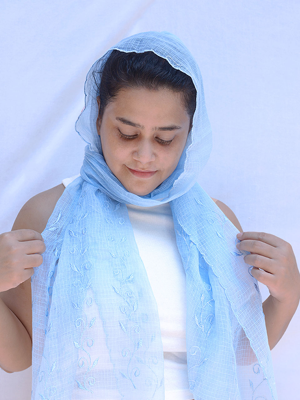 A woman elegantly draped in a light blue scarf, exuding grace and style.