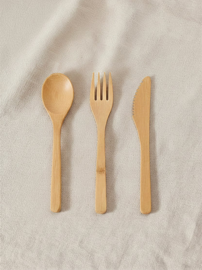 Bamboo spoon, fork, and knife on a beige fabric background