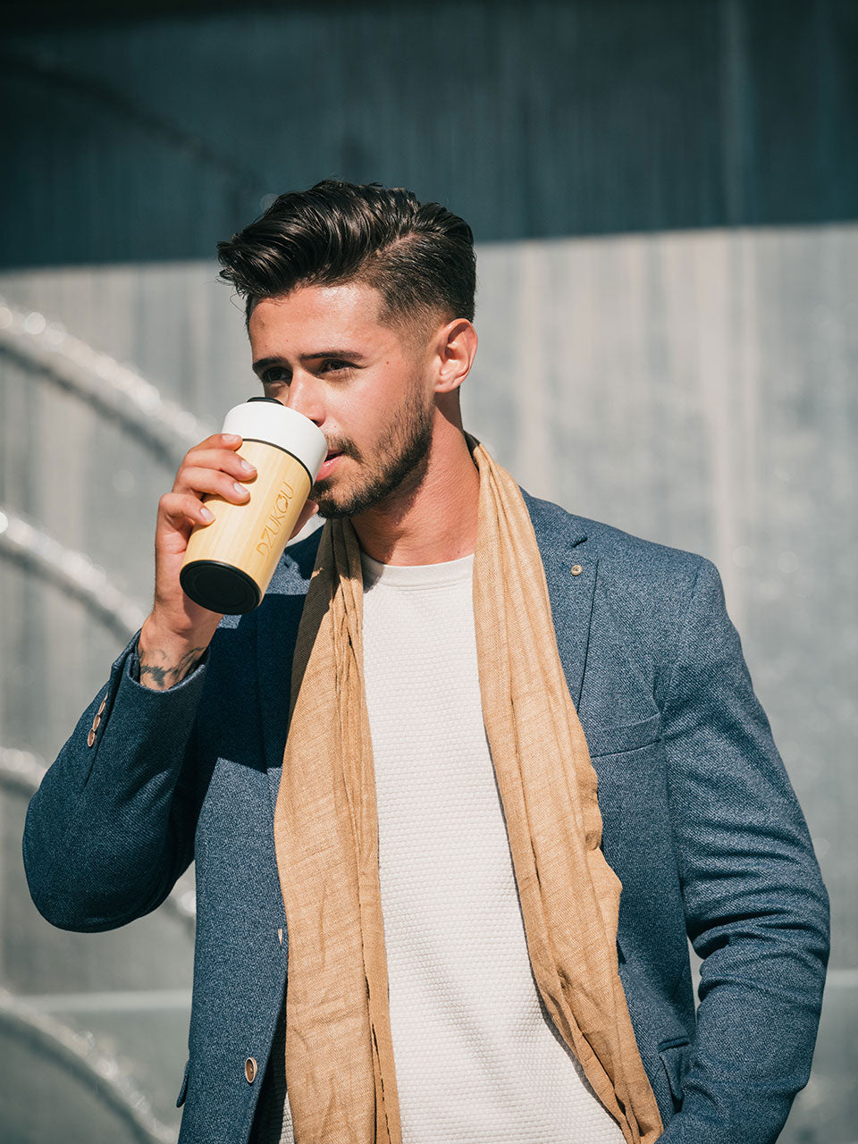 A man in a suit and a beige scarf enjoys a cup of coffee, exuding a sophisticated and relaxed demeanor.