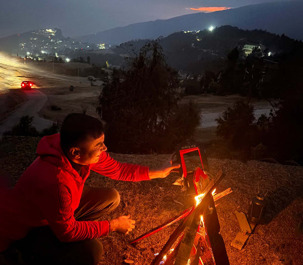Person lighting a campfire at night with a scenic background
