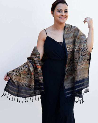 A woman in a black dress gracefully holds an ornate shawl, showcasing elegance and style.