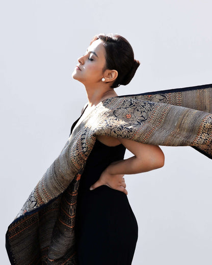 A woman in a black dress gracefully holds an ornate shawl, showcasing elegance and style.