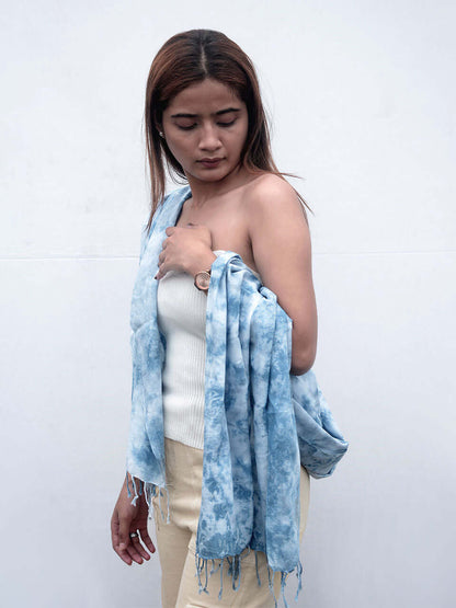 A woman elegantly draped in a blue tie-dye scarf, showcasing vibrant patterns and a stylish appearance