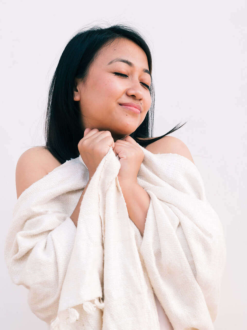 A woman draped in a soft, elegant white Eri silk shawl, showcasing its smooth texture and natural color.