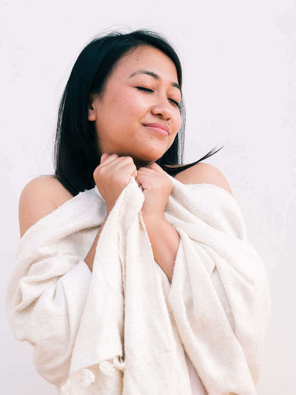 A woman draped in a soft, elegant white Eri silk shawl, showcasing its smooth texture and natural color.