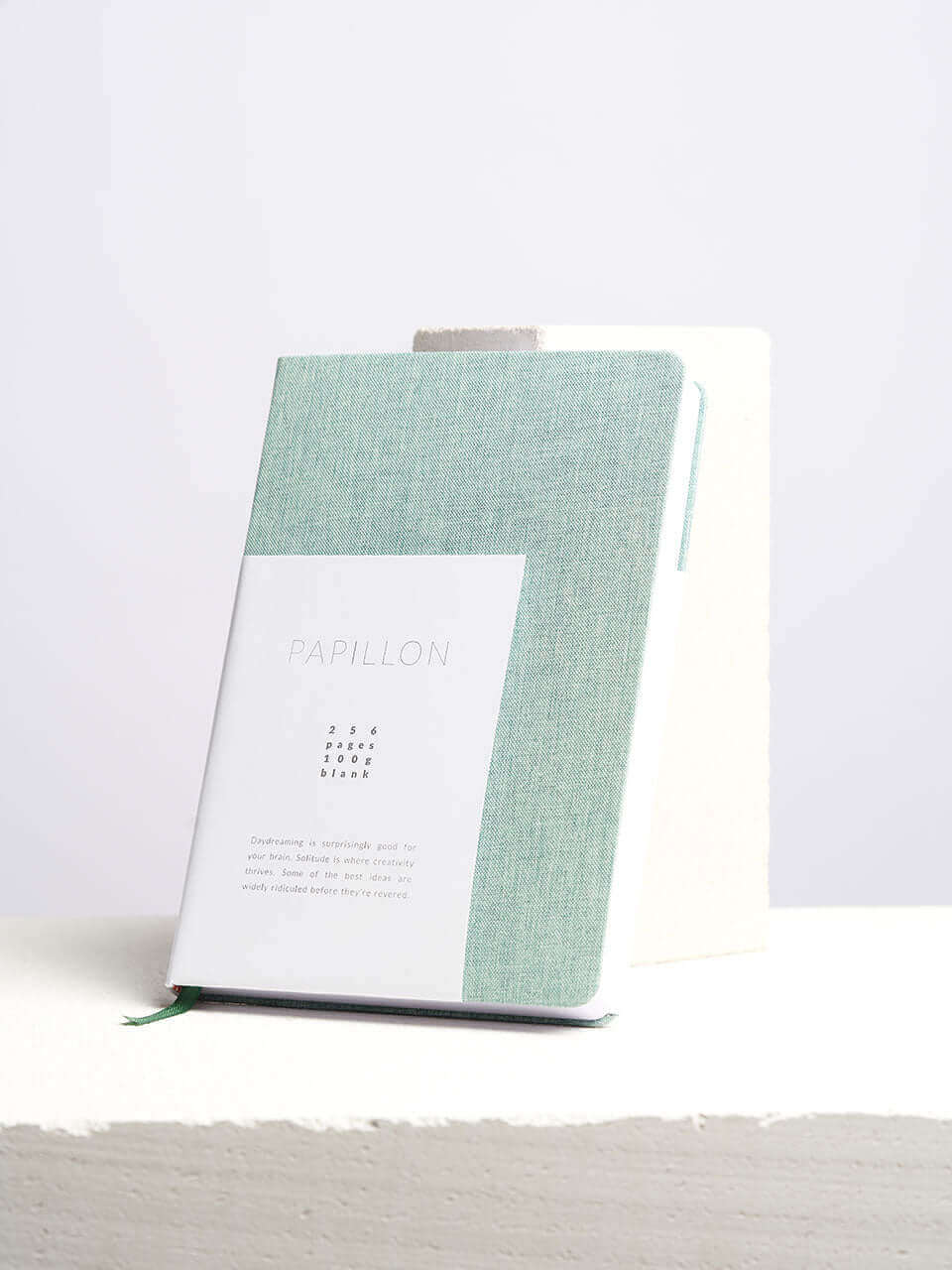 A linen notebook place beside a white block with a clean white background.