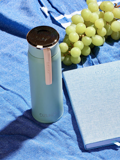 A bottle of water, a book, and a bunch of grapes arranged on a table, symbolizing relaxation and leisure reading.