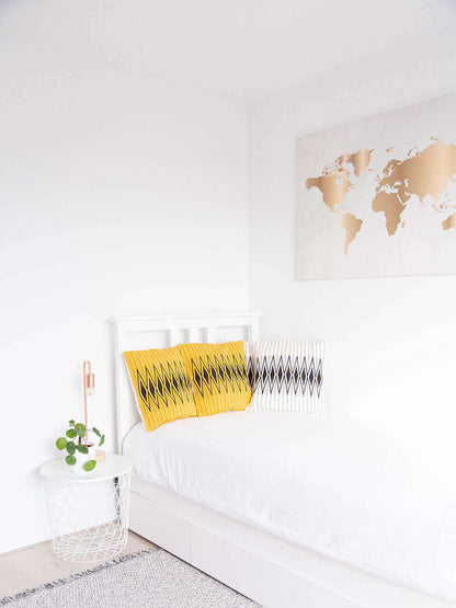 A white bed adorned with yellow and white pillow covers with beautiful black patterns, creating a vibrant and inviting atmosphere.